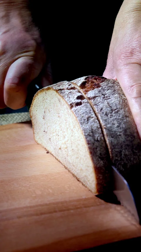 Vertical video, slow motion. Cutting dark bread into slices with a bread knife. Stock Footage 299641054