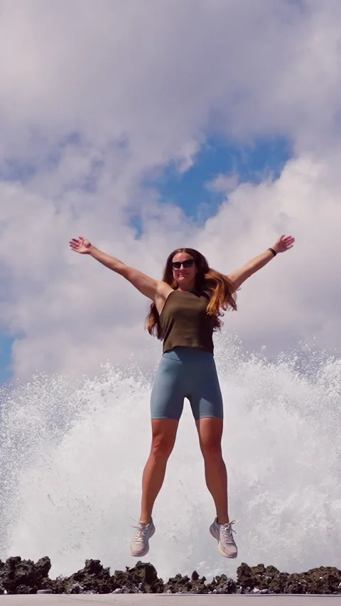 Vertical video. Slow Motion View of Woman Jumping in Front of Exploding Ocean Wa Stock Footage 336560550