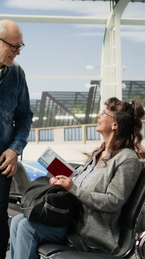 Vertical Video Smiling elderly man and woman sitting in airport lounge with Stock Footage 344373150