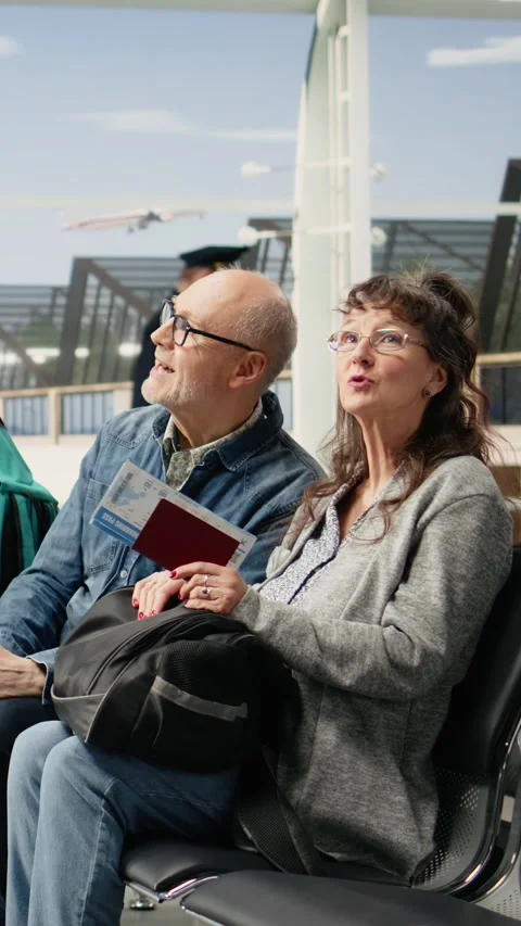 Vertical Video Smiling elderly man and woman sitting in airport lounge with Stock Footage 344373191
