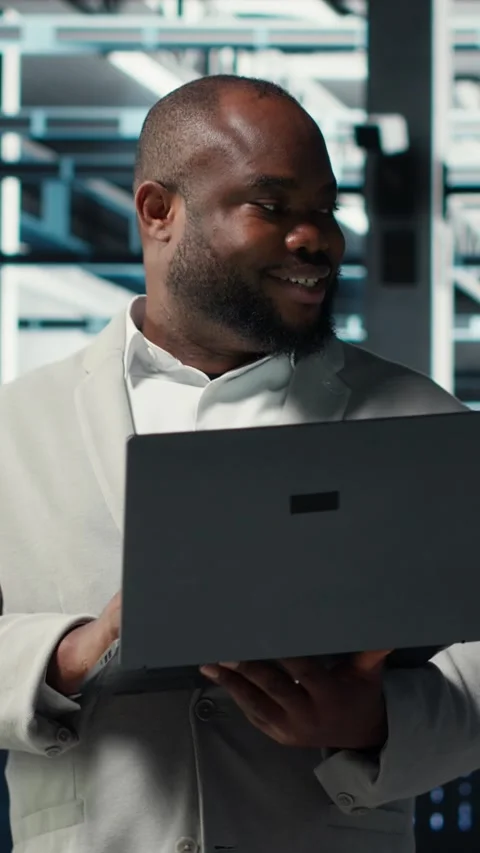 Vertical video Smiling engineer in data center managing software using laptop Stock Footage 311339081