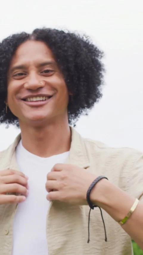 Vertical video: Smiling man adjusting beige overshirt and shifting left in park, Stock Footage 348728308