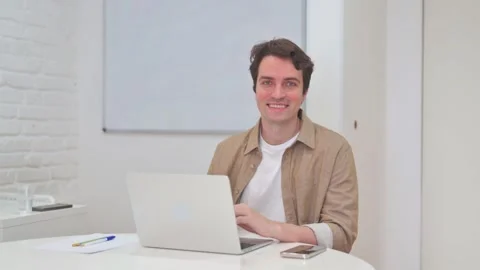 Vertical Video, Smiling Young Man Looking at Camera while Working on Laptop Stock Footage 312914335