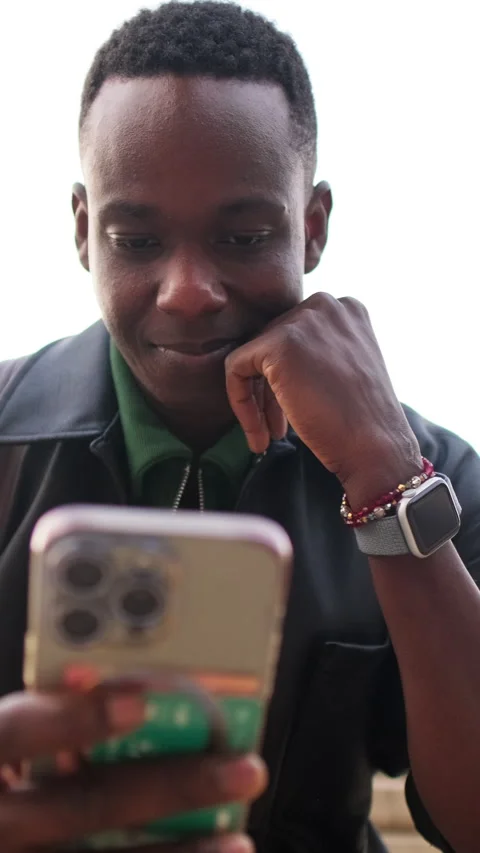 Vertical video, Smiling Young Man Using Phone Outdoors. Focus on the phone in Stock Footage 325633106