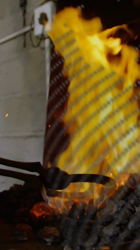 Vertical video: Smith nudging tongs into forge, causing flames forging metal Stock Footage 328350077