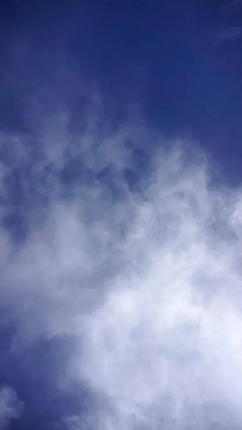 A vertical video of soft white clouds floating across a deep blue sky Stock-Footage 325710446