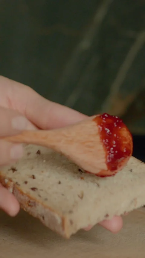 Vertical video Spreading raspberry jam on a slice of bread in a modern kitchen 스톡 동영상 323363835