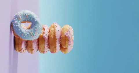 Vertical video of stack of donuts with pink and blue frosting on pink and blue Stock Footage 207400103