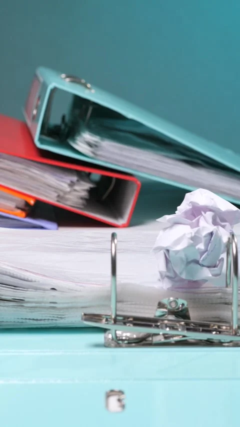 Vertical video stacked office binders and loose papers with a crumpled up paper Stock Footage 342771004