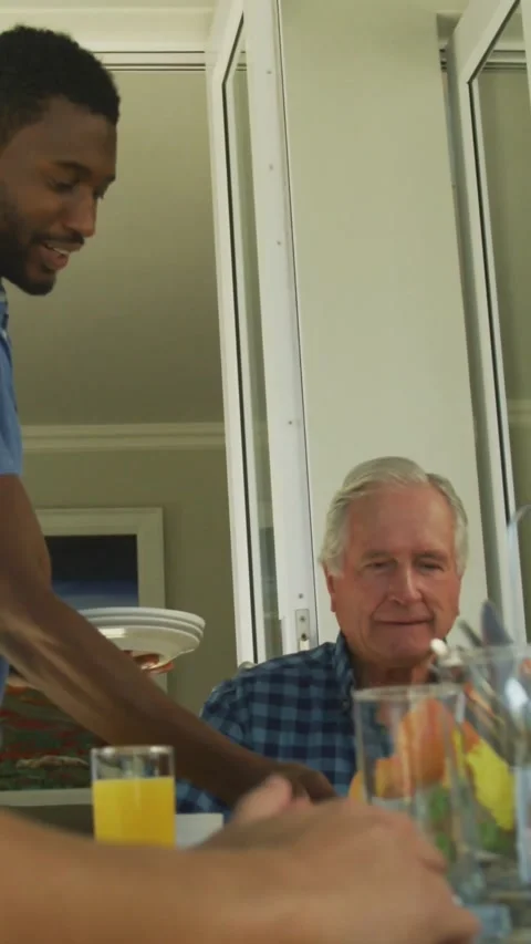 Vertical video: Standing man placing plates meal while senior watching tech Stock Footage 334319121