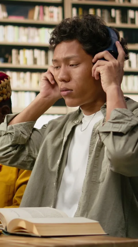 Vertical Video Student adjusting headphones at library study desk with computer Stock Footage 337528876