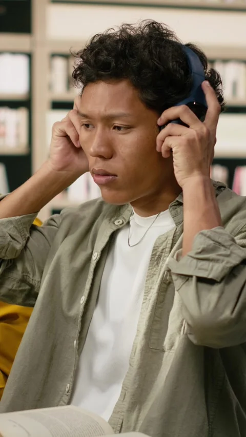 Vertical Video Student adjusting headphones at library study desk with computer Stock Footage 337530542
