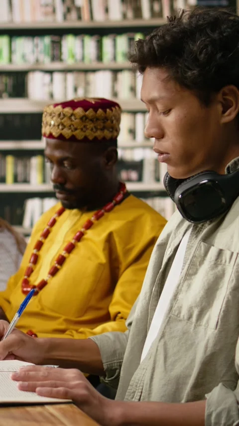 Vertical Video Student reading open book at library desk near chatbot on Stock Footage 337529269