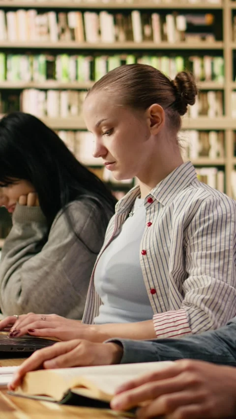 Vertical Video Student typing on laptop and taking notes from open book at Stock Footage 336378933