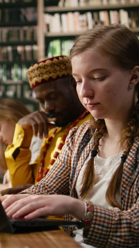 Vertical Video Student typing on laptop and taking notes beside open book at Stock Footage 337529402