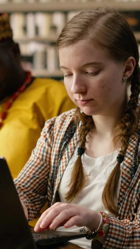 Vertical Video Student typing on laptop and taking notes beside open book at Stock Footage 337530924