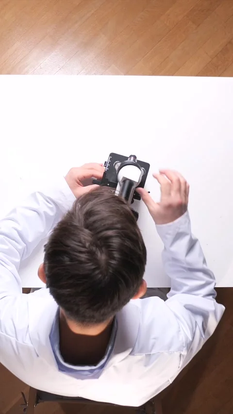Vertical video student in a white lab coat using a microscope on a white table Stock Footage 325902372