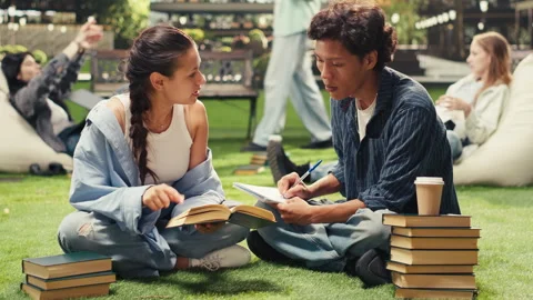 Vertical Video Students taking notes sitting on grass beside stacked books on Stock Footage 340797321