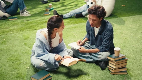 Vertical Video Students taking notes sitting on grass beside stacked books on Stock Footage 340805968