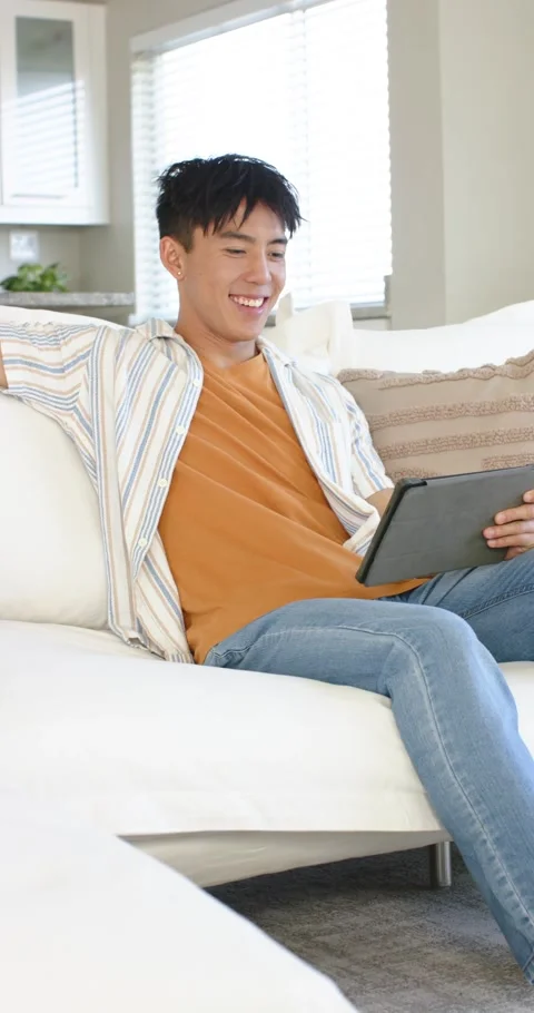 Vertical video: Studying tablet, swiping, Asian man smiling for relaxation on Stock Footage 345395814