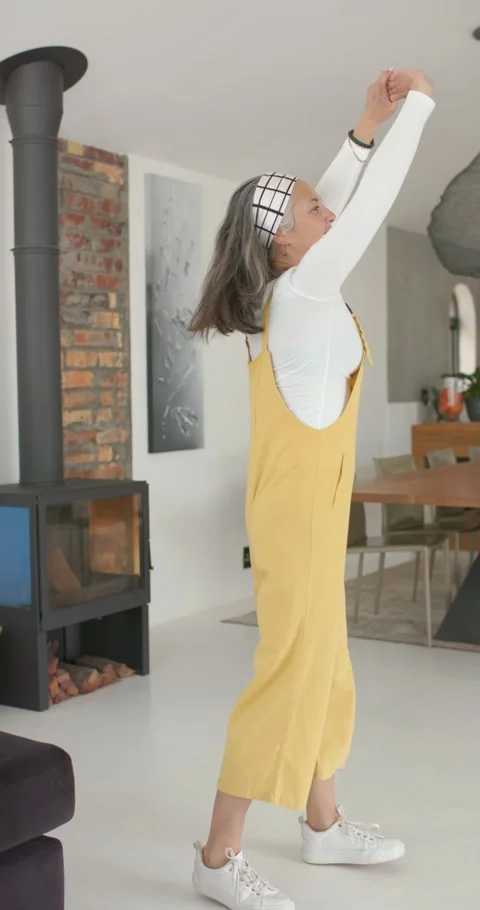 Vertical video: As sunlight streaming through window, senior woman stretching Stock Footage 345129619