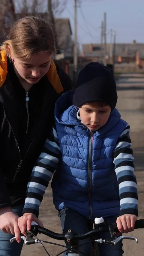 Vertical video. Supportive sister teaching younger brother to ride a bicycle Stock Footage 332528986
