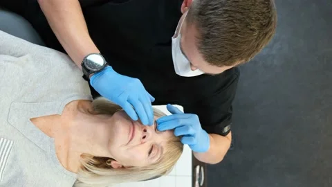 Vertical video, a surgeon examines the face of an old woman with his hands for Stock-Footage 222793002