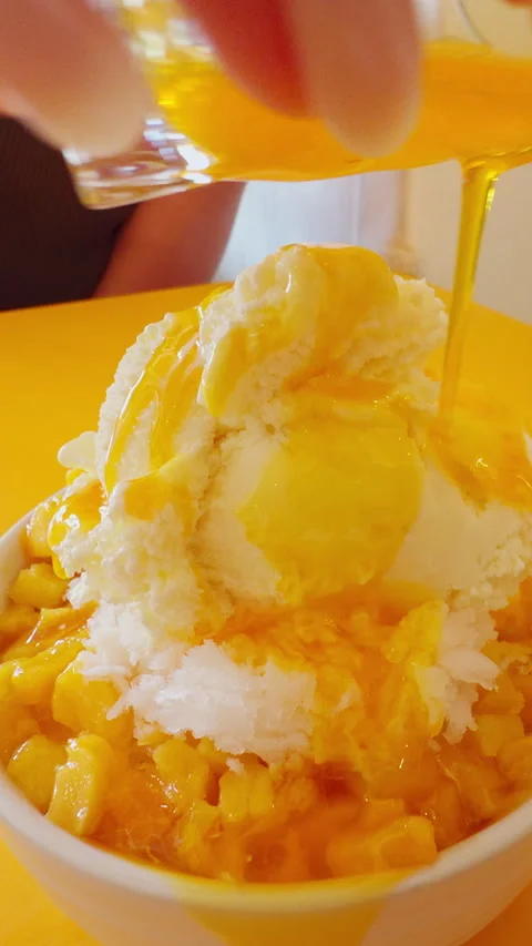 Vertical video. Sweet Mango Dessert With Shaved Ice And Cream Being Covered In M Stock Footage 337058111