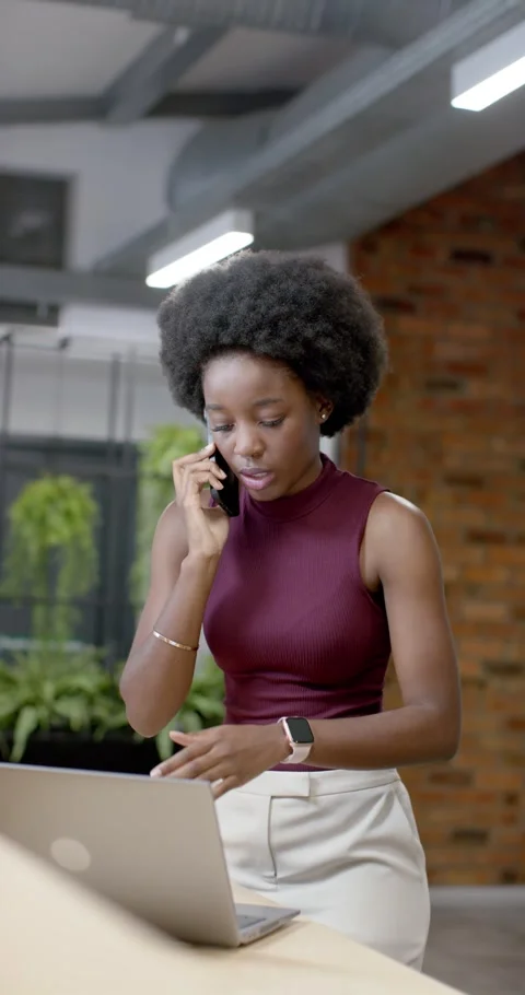 Vertical video: Taking call African American woman using cell and laptop at desk Stock Footage 342036036