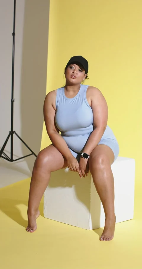 Vertical video: Taking cube seat before yellow backdrop woman posing adjusting Stock Footage 345491455