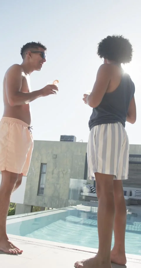 Vertical video: Talking two men at rooftop pool sun flaring relaxing in swimwear Stock Footage 345040819