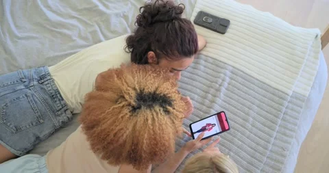 Vertical video: Tapping phone, three friends scrolling pink shopping app on bed, Stock Footage 345037185