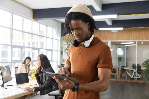 Vertical video: Tapping tablet, man standing in coworking wearing tan beanie and Stock Photos