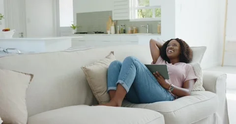Vertical video: Tapping tablet, woman in pink top reading and leaning on sofa at Stock Footage 341932826