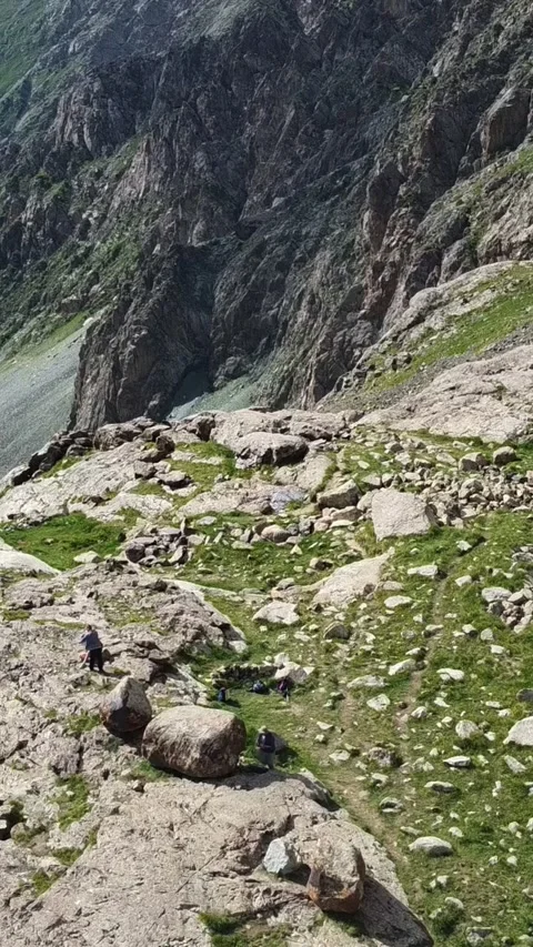 Vertical video: Tiny Hikers Trekking on Sunlit Mountain Slope Aerial Stock Footage 332221718