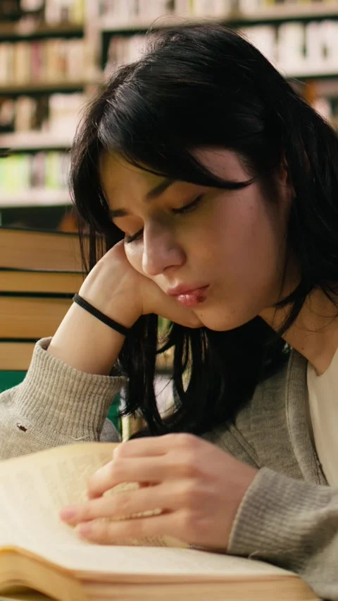 Vertical Video Tired student reading at busy library table with stacks of books Stock Footage 336379668