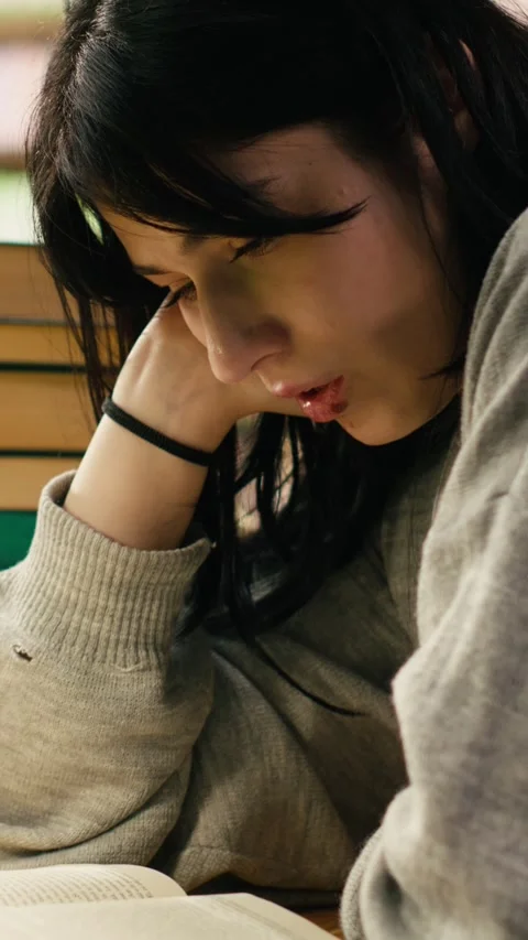 Vertical Video Tired student reading at busy library table with stacks of books Stock Footage 336380760