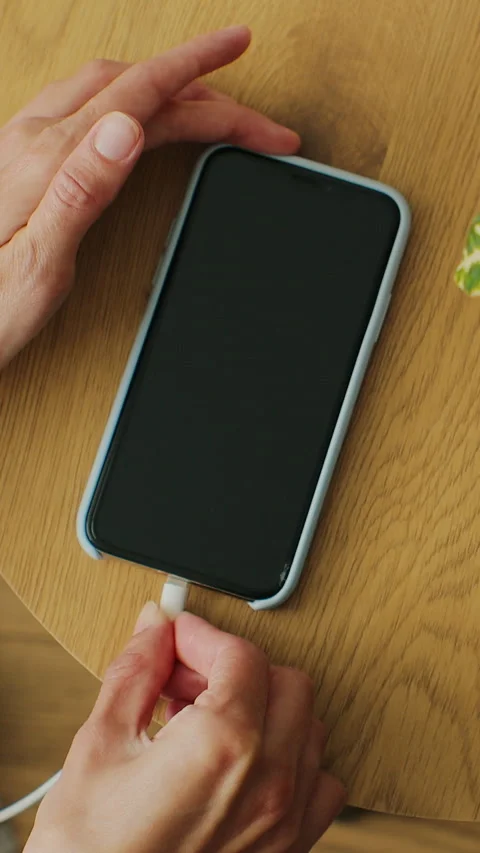 Vertical video. Top view. Hands of woman plugging charging cable in mobile phone 動画素材 347153105