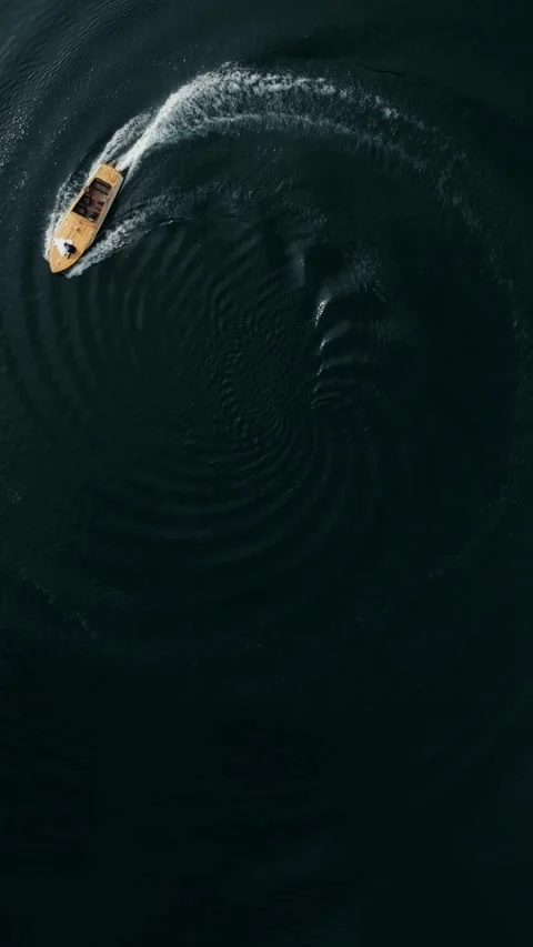 Vertical Video. Top view of the lake with a boat going in a spiral with Stock Footage 299840583
