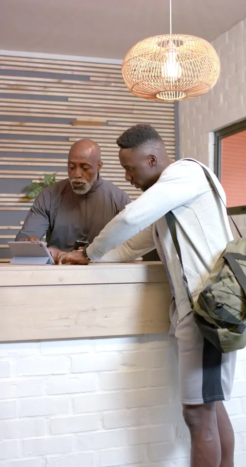 Vertical video: Two African American men entering lobby checking in using tablet Stock Footage 345320238