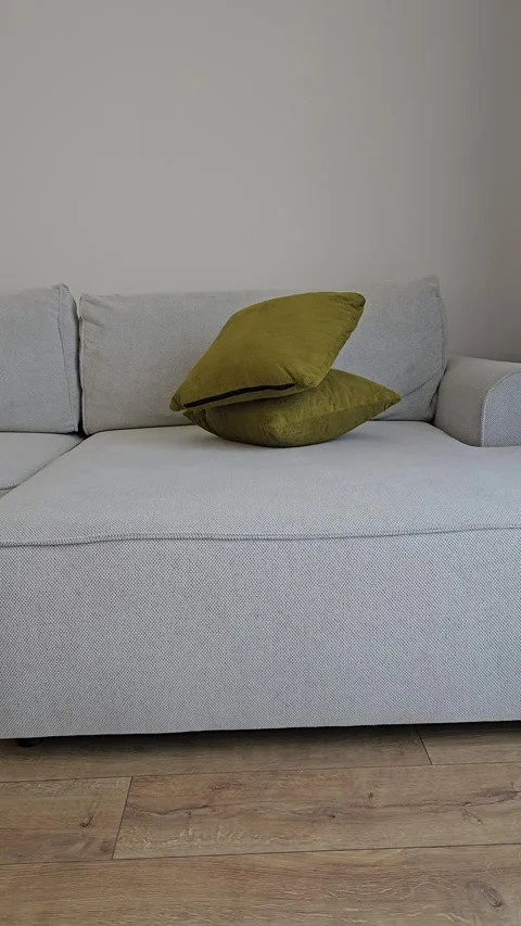 Vertical video of two bright olive green pillows falling onto a gray corner sofa Stock Footage 336947693