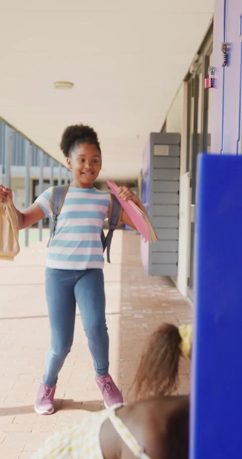 Vertical video of two happy, diverse schoolgirls talking by lockers in school Stock Footage 346723345
