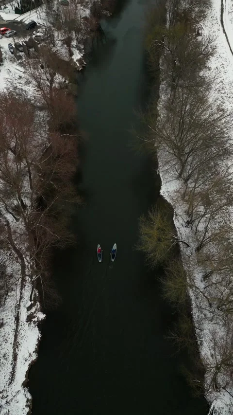 Vertical video. Two mans paddleboarding in a tranquil river with snowy trees Video stock 299541994