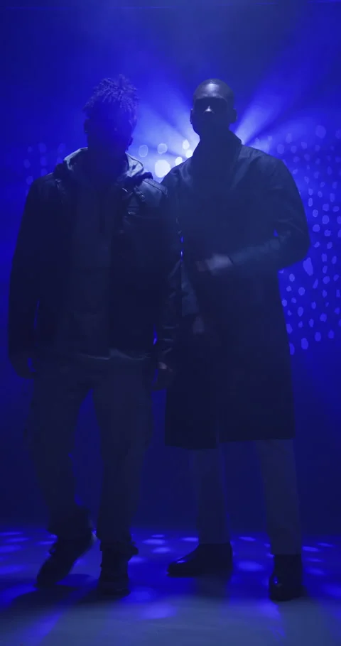 Vertical video: Two men in stylish outfits posing confidently under dramatic Stock Footage 310405651