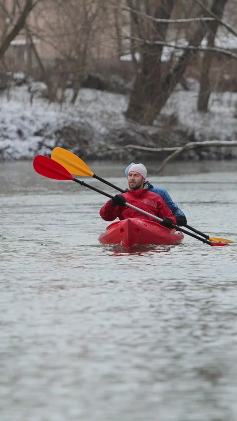 Vertical video. Two people kayaking on a calm river during winter with snowy Video stock 301553401