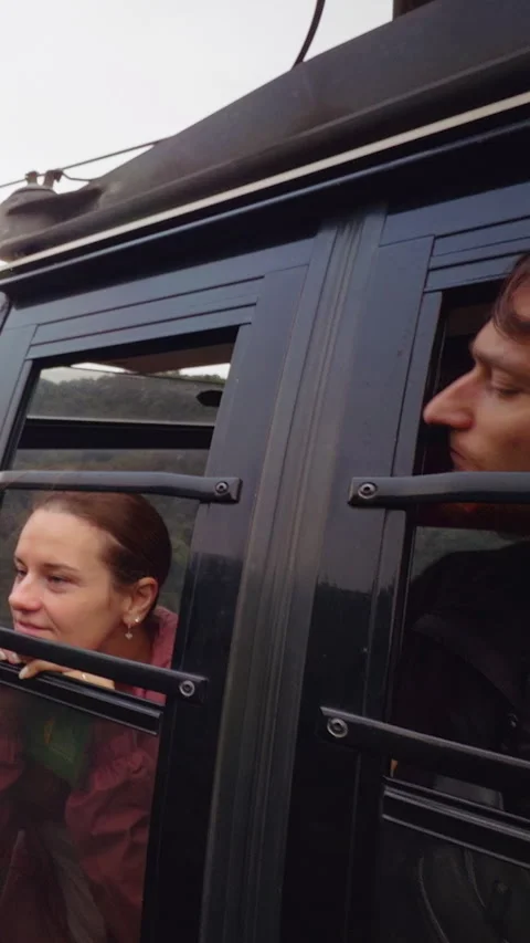 Vertical video. Two People Lean From Cable Car Window Looking Toward Forested Mo Stock Footage 323660159