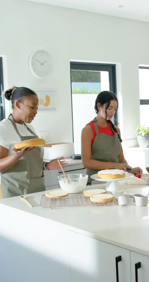 Vertical video: Two women making layer cake in kitchen left holding layer, right Stock Footage 346724428