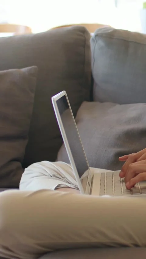 Vertical video: Typing person in light pants on gray sofa, hands starting to Stock Footage 348203367