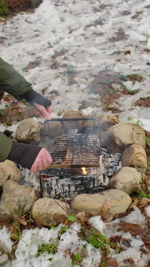 Vertical video of unknown young caucasian man puts grill on bonfire at winter Stock Footage 297943526