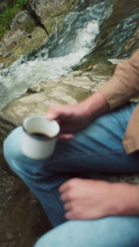 Vertical video of unknown young man drinking morning coffee by mountain river Stock Footage 285409431